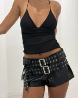 Shorts negros de efecto cuero con doble cinturón incorporado, con múltiples hebillas cuadradas plateadas y ojales metálicos.