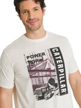 Remera de algodón color beige con cuello redondo y mangas cortas. Cuenta con un gran estampado gráfico frontal en tonos oscuros con la inscripción 'Power For' y 'Caterpillar', acompañado de una ilustración de maquinaria e infraestructura industrial.