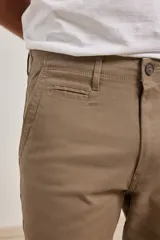 Pantalón de vestir verde oliva, de corte slim fit, sin pinzas, con bolsillos laterales y traseros. Se ajusta a la cintura con cinturón de cuero marrón.