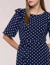 Vestido midi azul marino con estampado de lunares blancos, confeccionado en gasa semitraslúcida. Tiene escote redondo, mangas cortas acampanadas con volantes en los hombros, lazo ajustable en la cintura y falda con vuelo y forro interior.