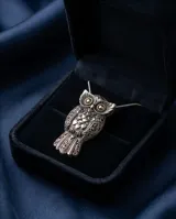 Dije con forma de búho elaborado en plata 925 con detalles en lámina de oro 18k en los ojos. Presenta un diseño detallado con texturas grabadas en las alas y el cuerpo.