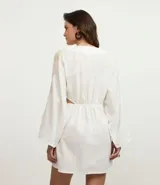 Vestido corto de playa confeccionado en voil de algodón BCI color blanco, con escote en V con lazo, cutouts laterales, mangas largas y bordados de caracoles de mar.