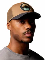 Gorro trucker Columbia Mesh Snap Back Hat, color marrón tostado con visera gris oscura y paneles traseros de malla. Cuenta con un parche gráfico redondo en el frente con diseño de montañas y cierre trasero ajustable.