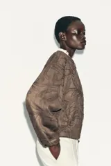 Chaqueta bomber color marrón con cuello redondo, manga larga con puño elástico y cierre frontal de cremallera metálica. Presenta un diseño de bordados florales en relieve por toda la prenda y bolsillos delanteros de vivo.