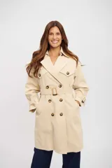 Trench coat color beige de corte clásico, con doble botonadura frontal, solapas anchas, cinturón ajustable con hebilla y trabillas en los puños.