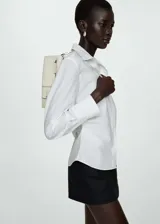 Camisa blanca de popelina de algodón con cuello camisero, cierre de botones, manga larga y detalles fruncidos.