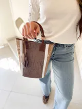 Bolso matero de cuero color taupe con textura croco y detalles en cuero color marrón. Tiene doble asa de mano y un dije de borla.