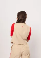 Chaleco beige con escote en V, sin mangas y cierre frontal con botones. Presenta pespuntes en color rojo y logo bordado en la espalda.