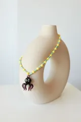 Collar corto con cuentas de plástico amarillas y verdes, y dije de vidrio con forma de pulpo negro.
