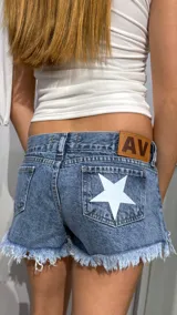 Short de jean de tiro bajo con ruedo deshilachado. Presenta una estrella blanca estampada en uno de los bolsillos traseros y una etiqueta de cuero sintético con las iniciales AV en la cintura.