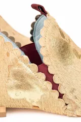 Botín de piel con acabado de pelo, color beige con estampado de manchas doradas. Presenta un diseño con bordes troquelados, aberturas laterales y detalle de borlón trasero en color granate. Incluye cuña interna y suela de cuero.