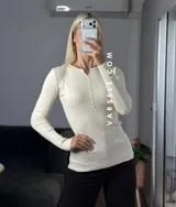 Remera de punto acanalado con escote redondo y cierre frontal parcial con botones. Presenta mangas largas y un ajuste entallado al cuerpo.