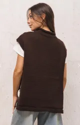 Chaleco tejido de punto color marrón, con cuello levemente alto, silueta amplia y aberturas laterales. Presenta un diseño de largo asimétrico, siendo más corto en el frente y más largo en la espalda.