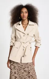 Trench corto Le Lis Blanc modelo Georgia, color beige, de corte recto, con cuello con solapa, doble botonadura frontal con botones carey, bolsillos delanteros con solapa y cinturón ajustable para la cintura.