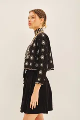 Saco corto de corte entallado con escote redondo, confeccionado en tejido negro con bordados artesanales de lentejuelas y pedrería en forma de estrellas y motivos florales en frente, espalda y mangas.