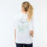 Camiseta blanca de corte oversize, con mangas cortas y cuello redondo, presenta un pequeño estampado gráfico en el pecho con la frase 'Sun & Limes'.