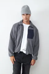 Campera de tejido polar tipo teddy en color gris, con cuello camisero, cierre frontal de cremallera y bolsillo funcional en el pecho con solapa de contraste.