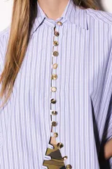 Camisa oversize a rayas celestes y blancas, con cuello camisero, manga larga y hilera de botones dorados metálicos.
