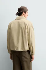Cazadora de corte relajado confeccionada en denim de algodón color beige. Presenta cuello solapa, cierre frontal con botones metálicos, bolsillos de vivo en la cadera y bajo ajustable con elástico. El interior cuenta con un forro estampado a contraste.