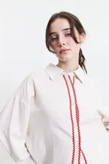 Camisa oversize color crema con detalles de puntilla roja en el frente.