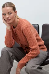 Cardigan de punto color naranja con diseño de rombos y trenzas en relieve. Presenta cuello redondo, cierre frontal con botones y mangas largas con puños ajustados.