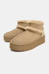 Botín plano de gamuza color beige, con interior y bordes forrados en pelo sintético. Presenta suela de plataforma engomada y tirador trasero.