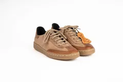 Zapatillas urbanas de cuero color taupe con detalles en terracota, cordones al tono y suela marrón.