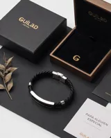 Pulsera de diseño masculino compuesta por una banda de cuerina trenzada en color negro y una placa central rectangular de acero inoxidable con acabado pulido.