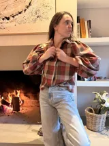 Camisa de color marrón oscuro con cuello clásico y mangas abullonadas con puños elásticos. Presenta un corte holgado y cierre frontal con botones.
