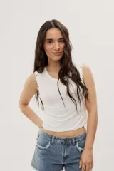 Top crop blanco de corte ajustado, con escote redondo, sin mangas y detalles de broches a presión metálicos en los hombros.