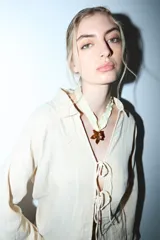 Camisa de manga larga color crema o beige claro, con textura arrugada, cuello camisero y cierre frontal mediante lazos anudados.