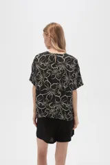 Blusa holgada de viscosa con estampado floral en tonos verde militar y blanco. Presenta cuello a la base, abertura frontal con botones y mangas cortas.