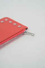 Billetera pequeña color negro con cierre de cremallera plateado y apliques de tachas metálicas redondas en la parte frontal.