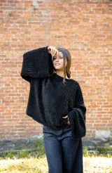 Buzo de textura tipo peluche en color negro, con diseño oversize, cuello amplio y mangas largas acampanadas.