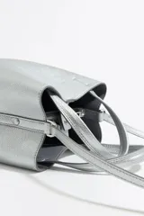 Bolso de mano pequeño color plateado, marca Bimba y Lola, modelo Chihuahua. Con doble asa de mano, asa larga ajustable y bolsillo interior con cremallera. Exterior personalizado con logo metálico.