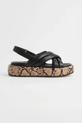 Sandalia de cuero ovino color negro, con tiras acolchadas cruzadas en el empeine y tira trasera con hebilla ajustable. Cuenta con una plataforma plana revestida con estampado de piel de serpiente.