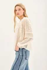 Camisa de manga larga confeccionada en tela plumeti, con cuello redondo, tajo delantero con cordones ajustables y volados verticales en el frente.