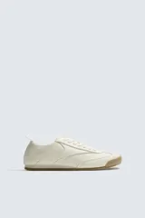 Zapatilla de estilo retro con cordones, confeccionada en piezas combinadas de color crema y suela dentada de goma en tono caramelo.