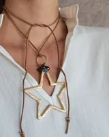 Collar tipo gargantilla con tiento de cuero marrón y dije de estrella grande en metal dorado con textura martillada. Incluye detalles de cuentas de cristal en tonos azul y marrón.