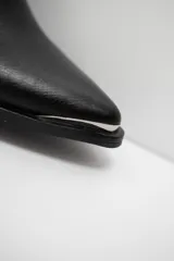 Bota bucanera de cuero color marrón oscuro, con taco cuadrado de 6 cm y punta fina con detalle metálico. Presenta una tira vertical decorativa con tachas metálicas en la parte superior de la caña.