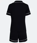 Conjunto de pijama corto negro con ribetes blancos, compuesto por una camisa de manga corta con cuello, bolsillo en el pecho y cierre abotonado, y un short con cintura elástica.