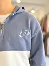 Hoodie de felpa con capucha y medio cierre frontal, diseño en bloques de color celeste y blanco, con bordados decorativos en el pecho.