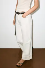 Jeans blancos de tiro medio y corte barrel con pernera holgada que se estrecha hacia el tobillo, terminando con un dobladillo vuelto con costuras visibles. Cuenta con diseño de cinco bolsillos y cierre frontal con cremallera y botón metálico.