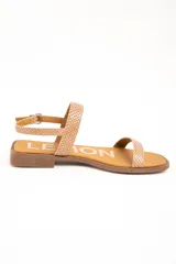 Sandalias planas de cuero color beige con estampado tipo animal print de serpiente texturado. Posee una tira delgada en la parte delantera y una tira ajustable con hebilla metálica alrededor del tobillo, sobre una suela plana y punta cuadrada.