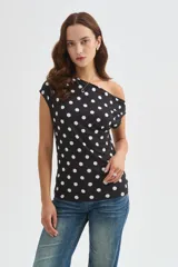 Top de poliéster negro con estampado de lunares blancos, diseño al cuerpo y cuello asimétrico de manga corta.
