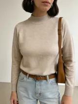Buzo de punto en color beige, con cuello redondo alto y mangas largas con diseño raglán. Presenta puños y cuello acanalados.