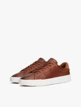 Zapatillas de estilo tenis Tommy Hilfiger confeccionadas en piel color marrón, con diseño de corte bajo, cordones al tono y suela de goma blanca. Presenta un panel de gamuza a contraste en el talón y el logo de la marca grabado en el lateral.