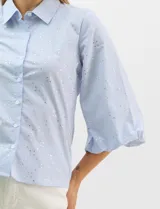 Camisa de algodón con patrón de rayas verticales, cuello camisero clásico y cierre frontal con botones. Presenta detalles metálicos aplicados en el frente y mangas, con mangas 3/4 abullonadas y ruedo recto.