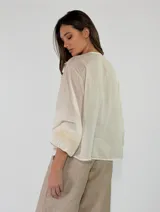 Blusa de algodón blanca con escote en V, mangas largas amplias y detalles de volados con encaje bordado en el frente.