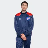Conjunto deportivo Umbro del Club Nacional de Football, compuesto por una campera con cierre frontal y pantalón de jogging a juego. La campera es azul con detalles en rojo en los hombros y el logo de Umbro y el escudo del club en el pecho. El pantalón es azul con el escudo del club en el muslo.
